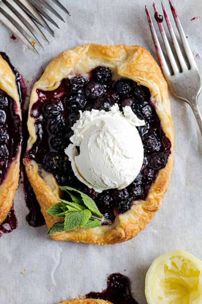 These sweet little vegan rustic tarts are full of sweet blueberries, lemon and mint wrapped in light, flaky puff pastry. They're so easy to make for a quick and delicious dessert! #rustictart #vegantarts #blueberries #veganrecipes #vegandessert #blueberrytart | Recipe on thecookandhim.com