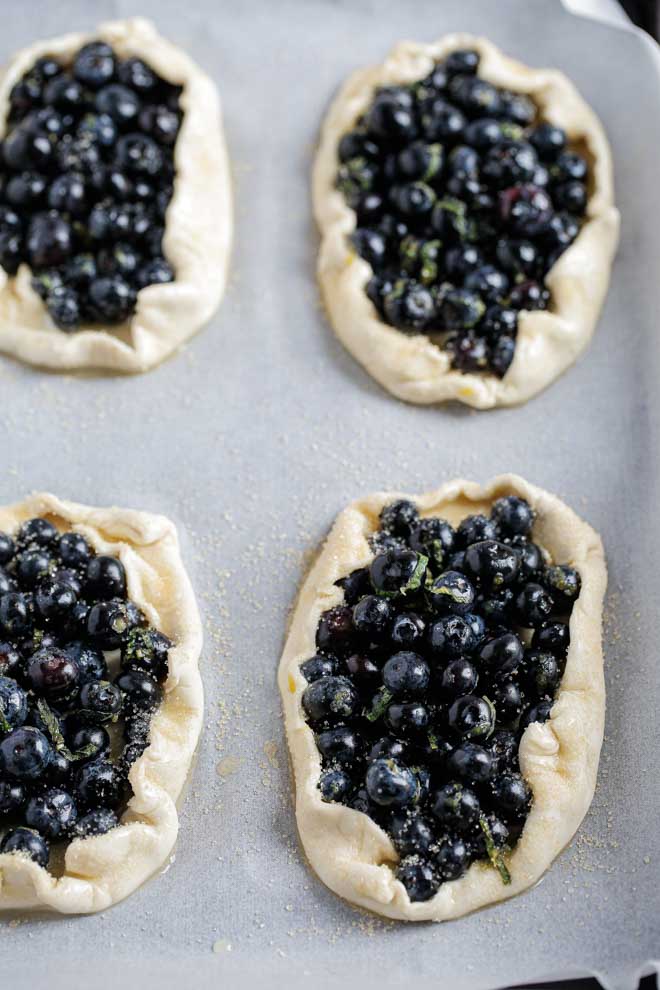 These sweet little vegan rustic tarts are full of sweet blueberries, lemon and mint wrapped in light, flaky puff pastry. They're so easy to make for a quick and delicious dessert! #rustictart #vegantarts #blueberries #veganrecipes #vegandessert #blueberrytart | Recipe on thecookandhim.com