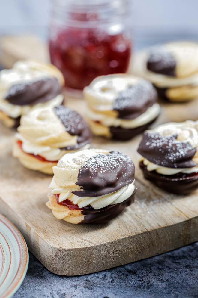 Light buttery vegan viennese whirls, dipped in dark chocolate and sandwiched with jam and buttercream. The perfect afternoon treat! #vegancookies #veganbaking #viennesewhirls #veganrecipe #butterbiscuits #howtomakeviennesewhirls | Recipe on thecookandhim.com