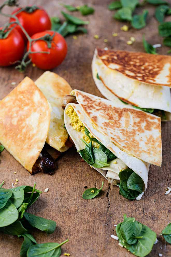 This folded breakfast wrap might not change your world but it'll definitely change the way you see folding wraps! This vegan breakfast version is filled with tofu eggs, vegan sausage, bacon and cheese, spinach and tomato. It's super easy, filling and SO delicious to eat! #breakfastwraps #veganbreakfast #vegansausages #veganbacon #tofuscramble #tofueggs #plantbased #highproteinveganbreakfast | Recipe on thecookandhim.com