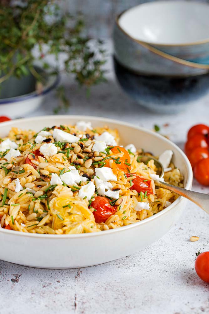 An easy summer dinner with gorgeous pops of flavour in every bite! The lemon and herb orzo is mixed with roasted cherry tomatoes and topped with toasted pine nuts and vegan feta cheese | Recipe on thecookandhim.com | #orzo #pasta #veganpasta #veganmeal #plantbased #vegancheese #dairyfree