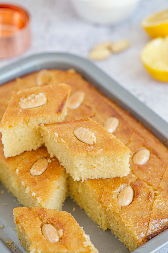 A traditional Middle Eastern cake make with a base of semolina and yoghurt, Basbousa is sweet, light and fragrant and so so moist! It's also studded with almonds and soaked after cooking in a sticky lemon syrup | Recipe on thecookandhim.com #basbousa #semolinacake #vegan #vegancake #eggfreecake #dairyfree #veganbaking