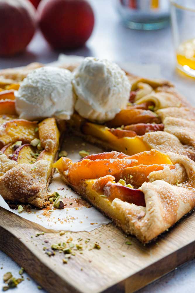 This easy, vegan peach tart is summer in every bite! Super simple homemade pastry brimming with fresh, juicy peaches served warm with a sweet orange and cardamom drizzle | recipe on thecookandhim.com | #vegan #vegandessert #peachtart #summertart #peaches #veganbaking #veganrecipe #veganpastry