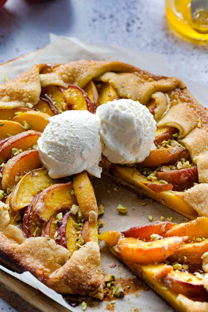 This easy, vegan peach tart is summer in every bite! Super simple homemade pasty brimming with fresh, juicy peaches served warm with a sweet orange and cardamom drizzle | recipe on thecookandhim.com | #vegan #vegandessert #peachtart #summertart #peaches #veganbaking #veganrecipe #veganpastry