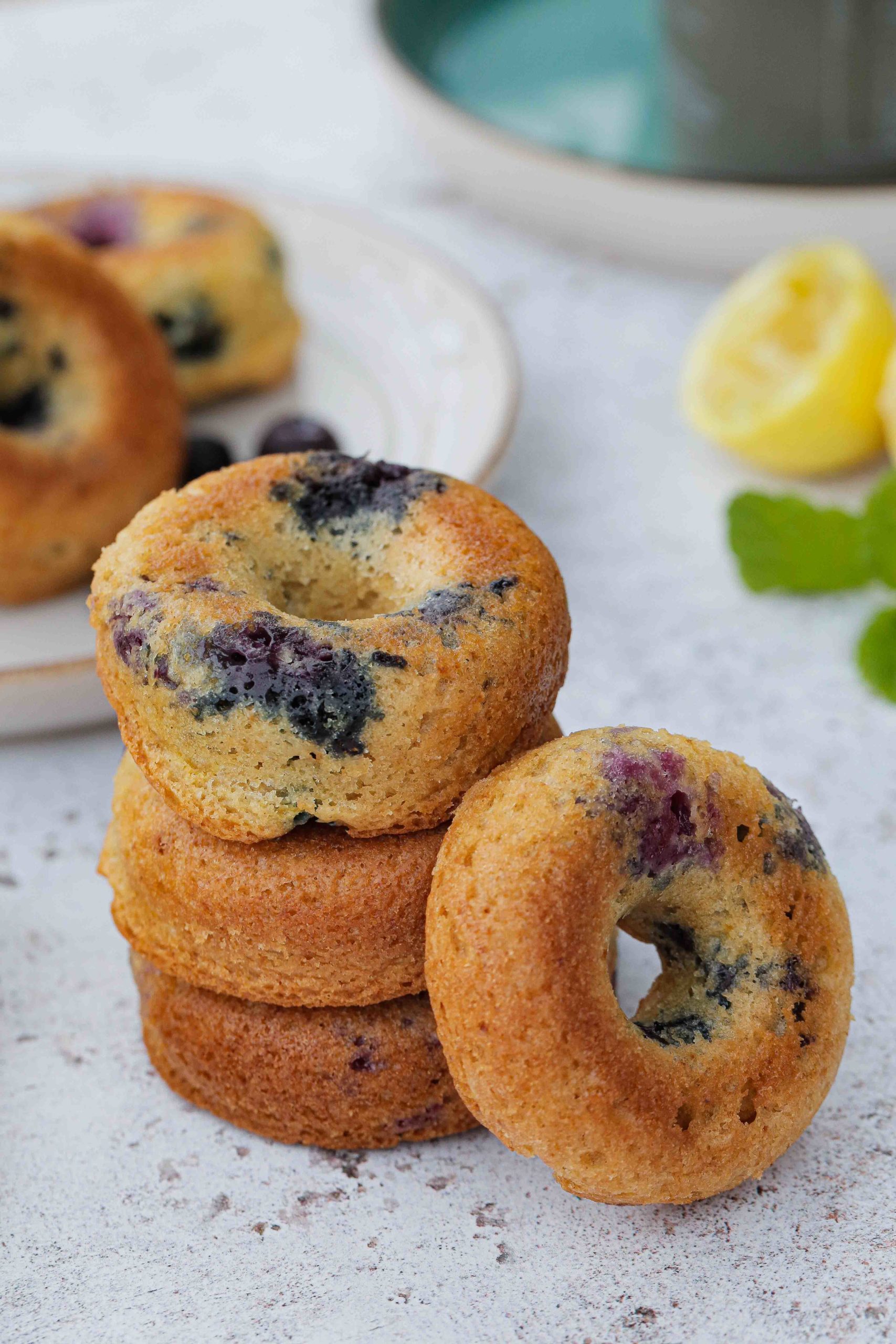 These baked donuts, flavoured with lemon and studded with juicy blueberries are squidgy perfection! They're non yeast, more cake donuts which means they're super simple and quick to make. Absolutely delicious warm or cold with a cuppa for breakfast or an afternoon vegan treat! Recipe on thecookandhim.com #vegandonut #bakeddonuts #homemadedonuts #cakedonuts