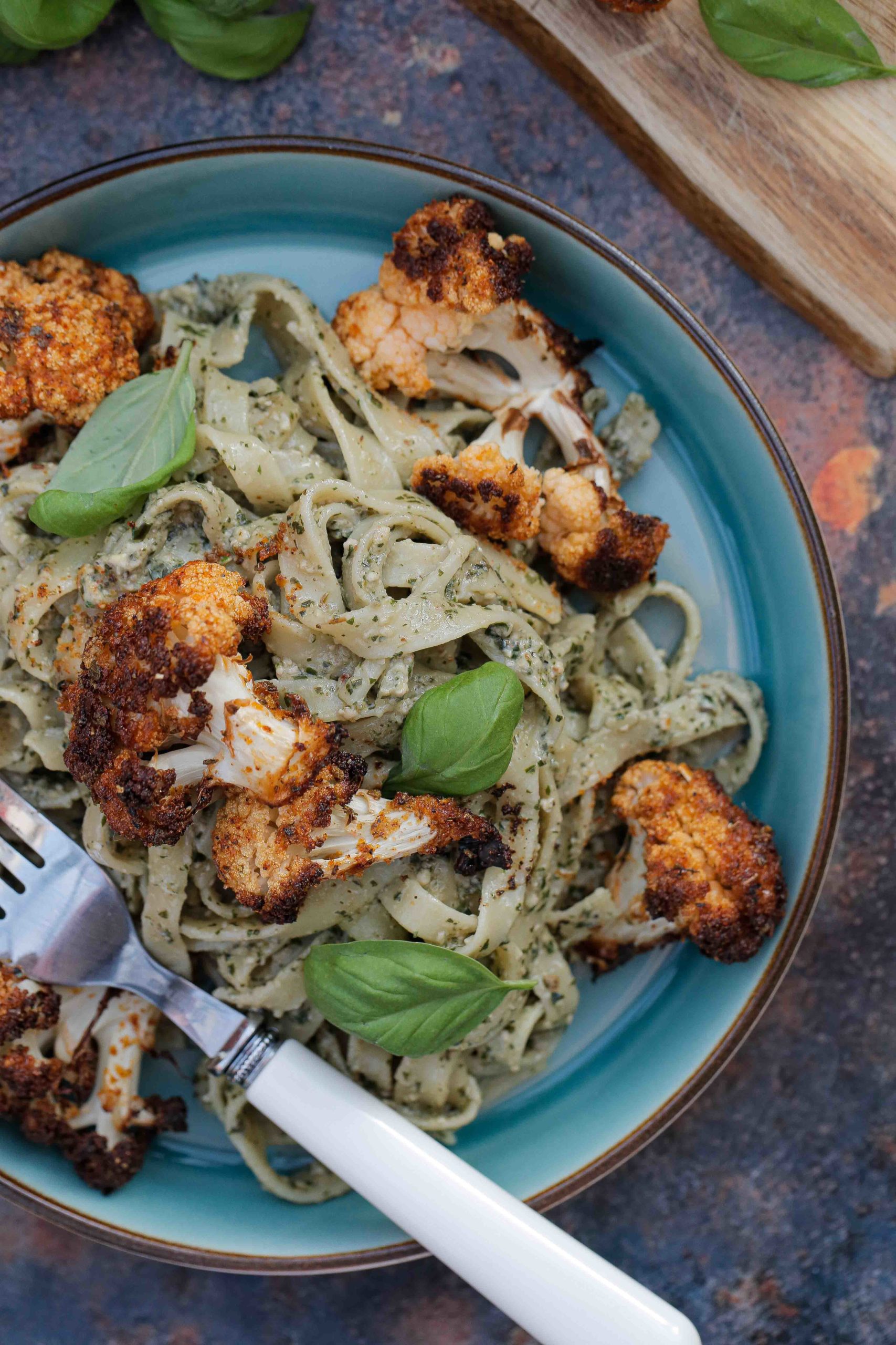Herby basil pesto stirred through tagliatelle and topped with lightly spiced crispy roast cauliflower. A lovely contrast of textures and flavours that work perfectly together for an easy weeknight meal or date night deliciousness! Recipe on thecookandhim.com | #veganpesto #roastcauliflower #veganmeal #vegandinner #cauliflowerrecipes