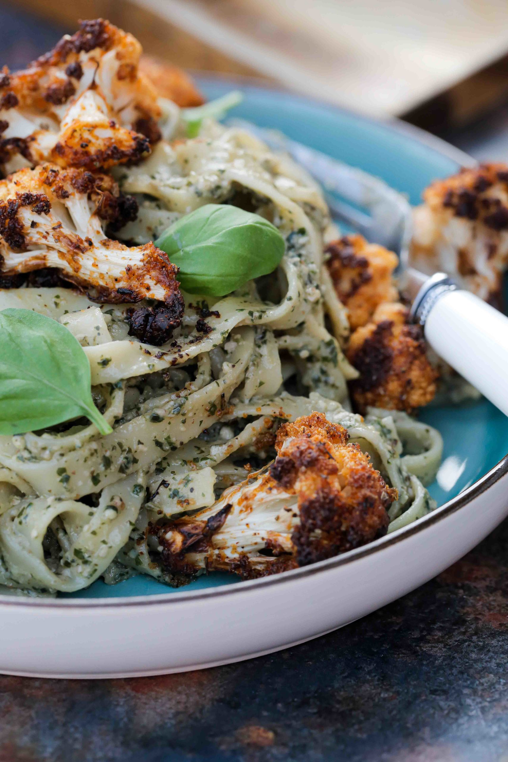 Herby basil pesto stirred through tagliatelle and topped with lightly spiced crispy roasted cauliflower. A lovely contrast of textures and flavours that work perfectly together for an easy weeknight meal or date night deliciousness! Recipe on thecookandhim.com | #veganpesto #roastcauliflower #veganmeal #vegandinner #cauliflowerrecipes