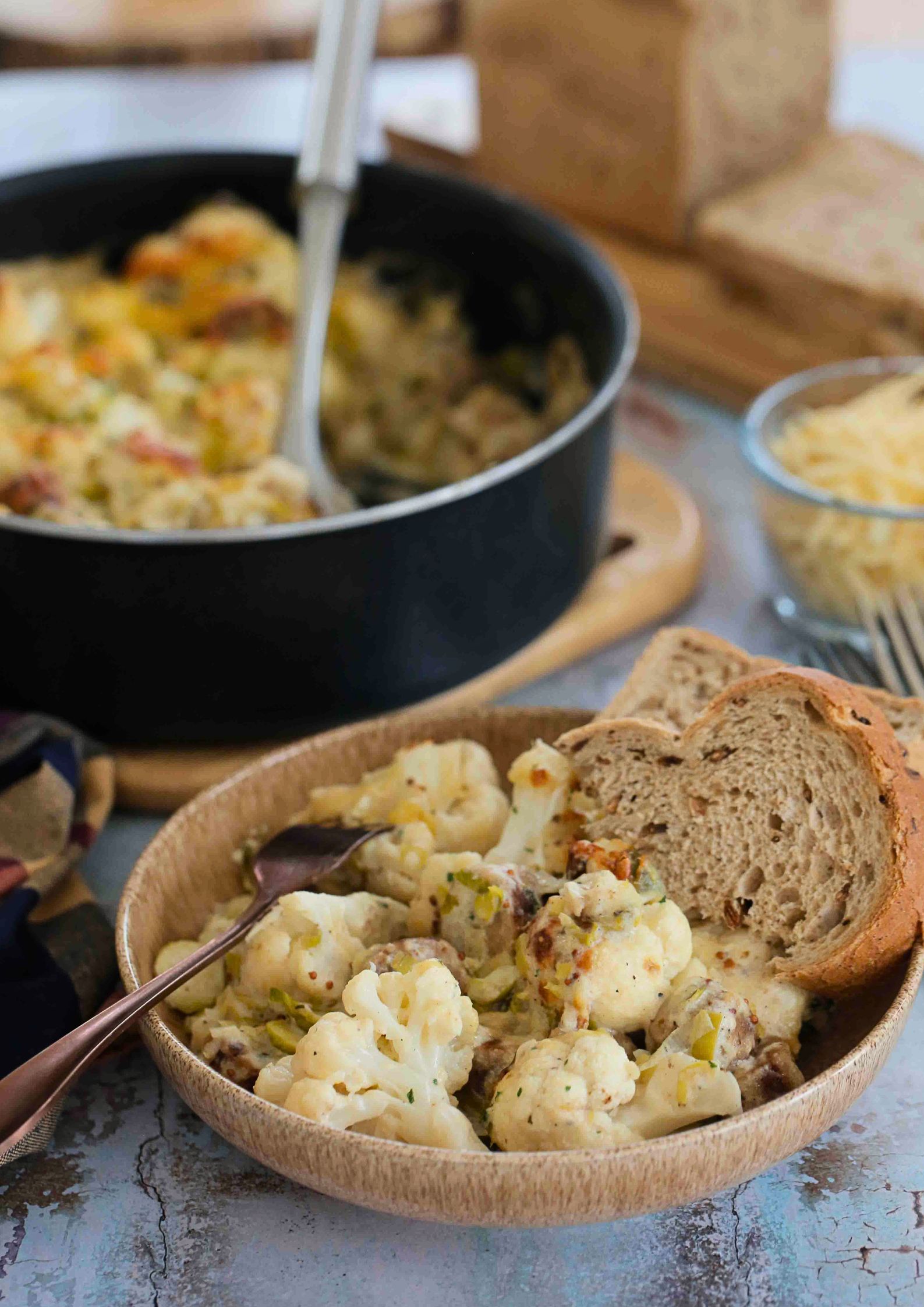 Baked until crisp and bubbly, this vegan cauliflower cheese with leeks, sprouts and sausages is a whole meal all cooked in one pan for an easy dinner! Recipe on thecookandhim.com | #cauliflowercheese #easydinner #onepanmeal #quickdinnerideas #easyveganmeals