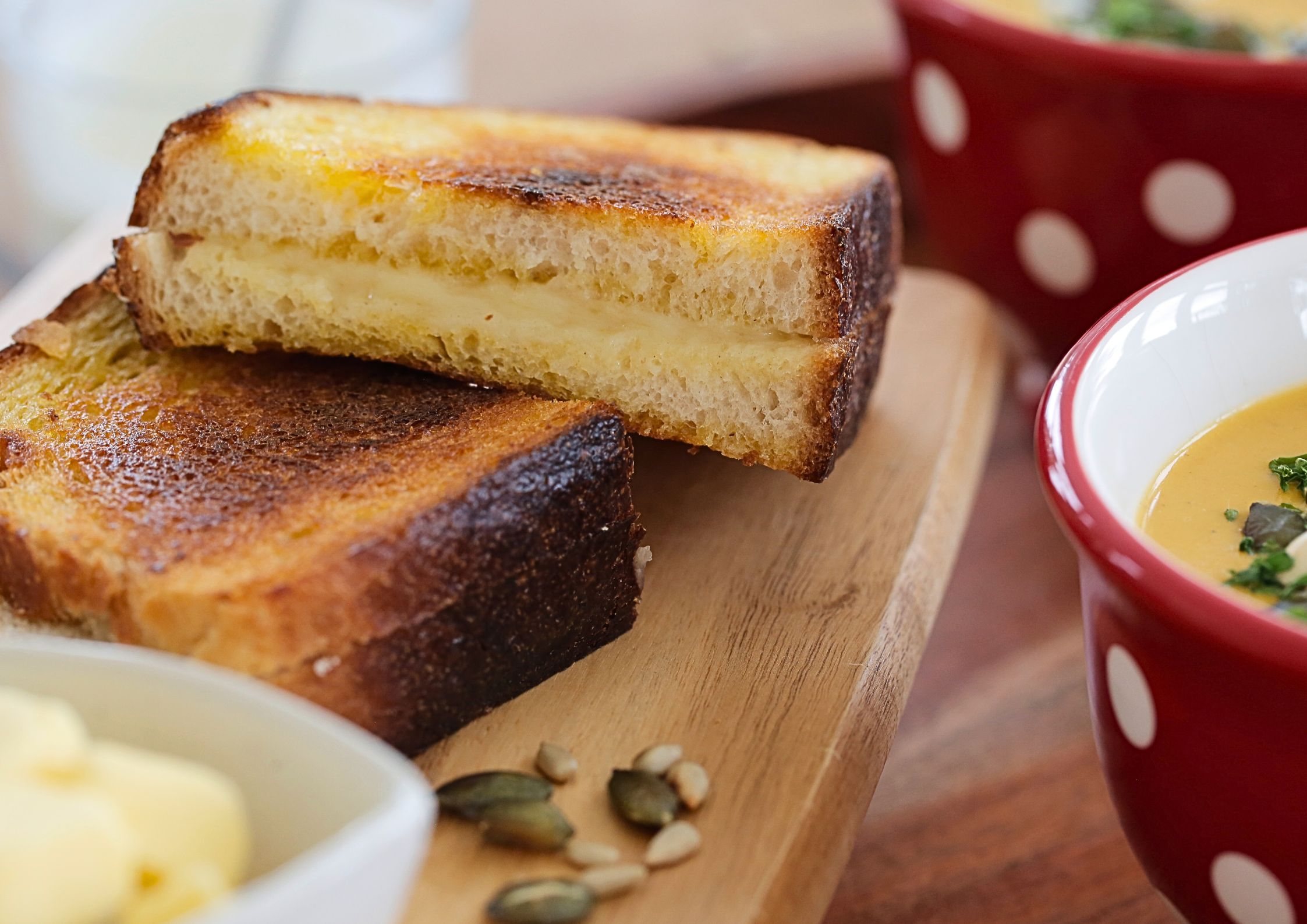 A close up photo of a toasted sandwich filled with melted cheese. To the side are two bowls of soup