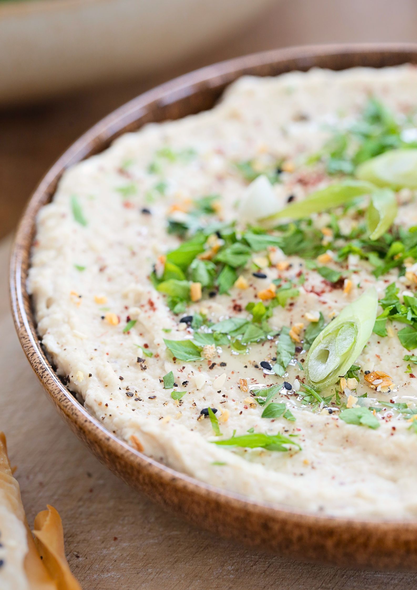 A close up of white bean dip dressed with herbs, spices and spring onions