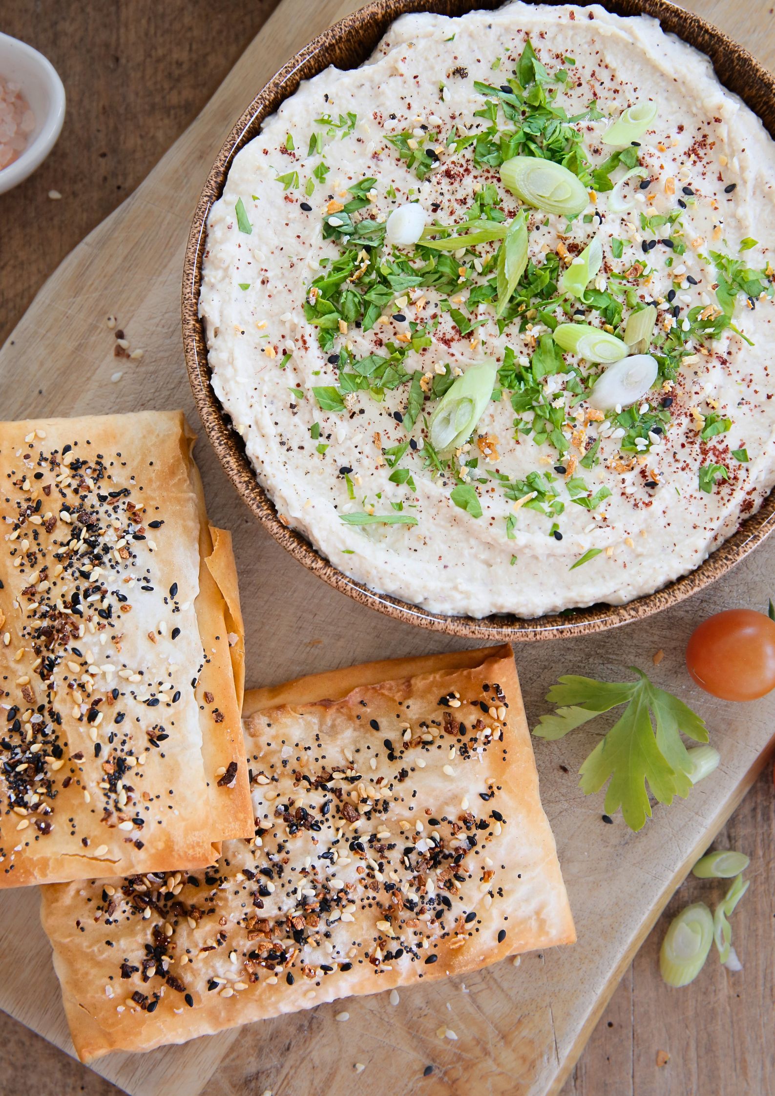 A close up of white bean dip dressed with herbs, spices and spring onions and 2 crispy filo parcels coated in mixed seeds