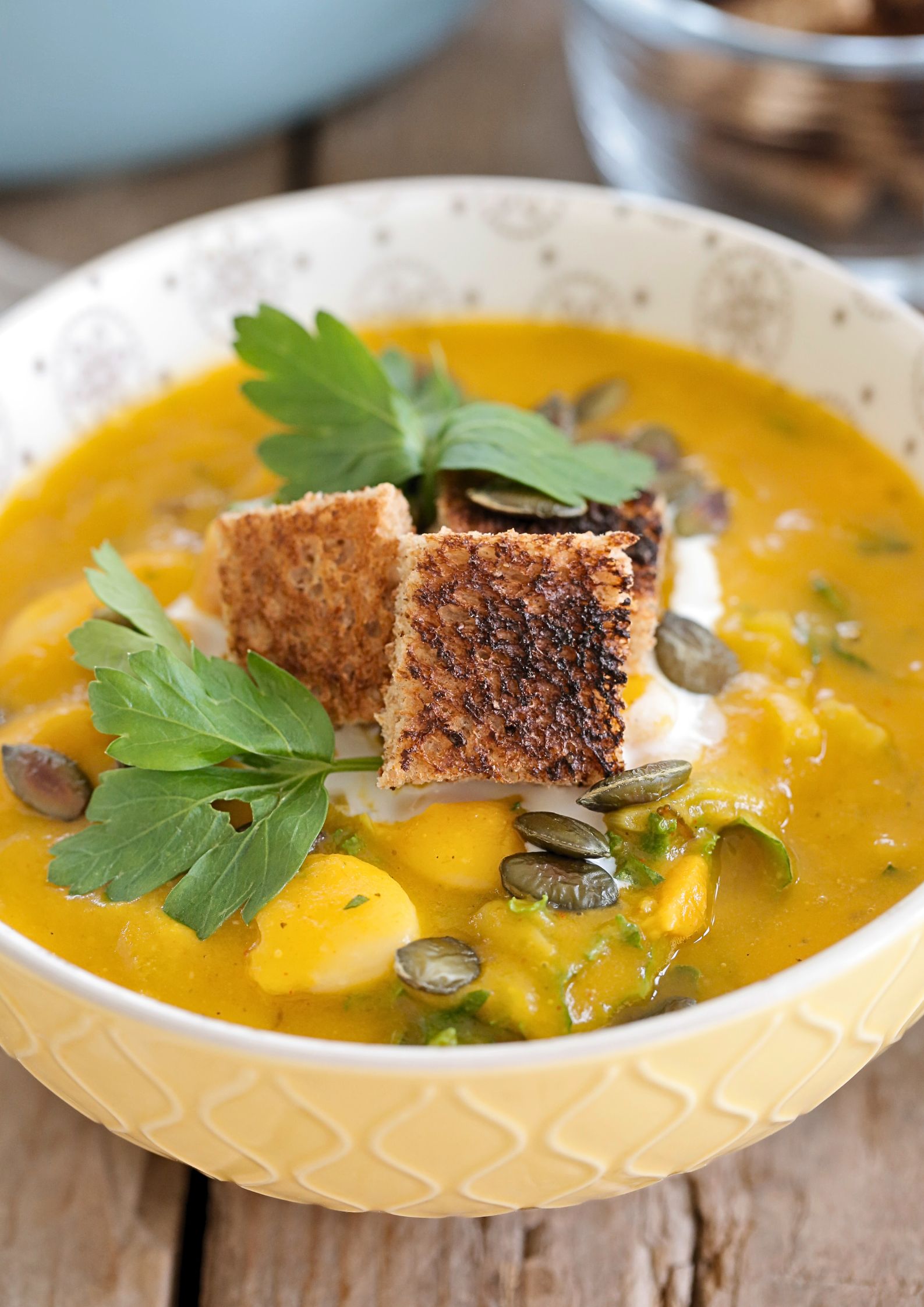 A close up photo of a bowl of autumn vegetable soup garnished with crisp croutons and fresh green herbs