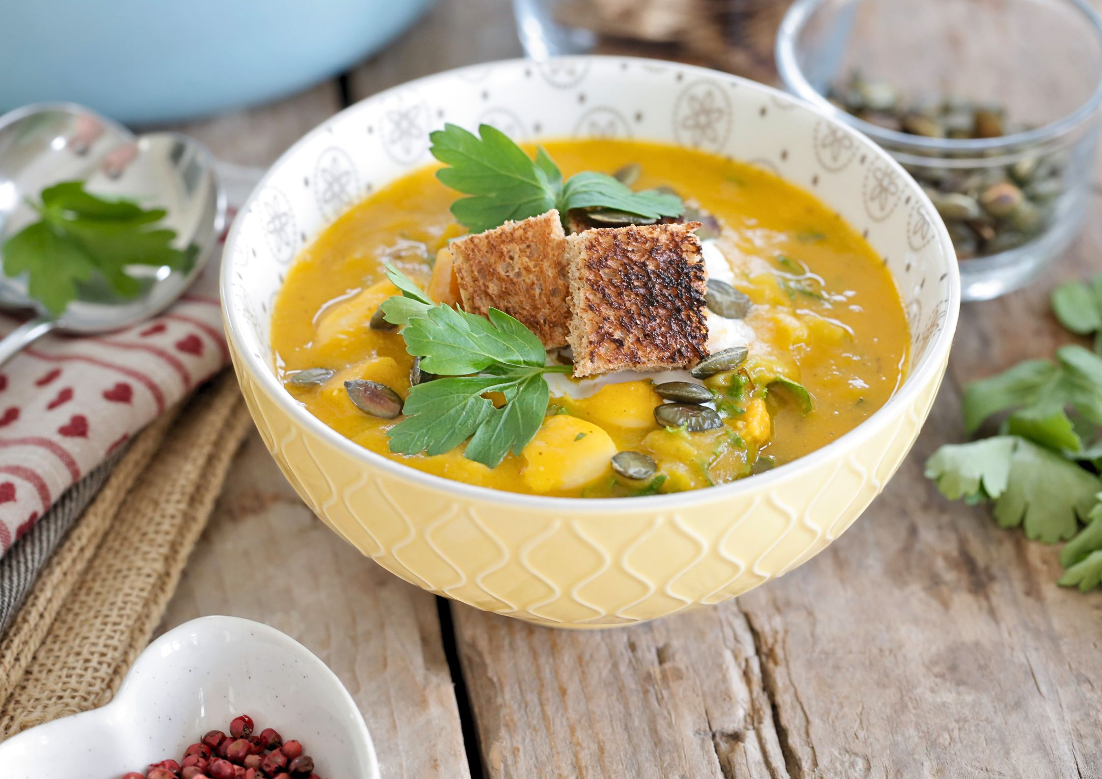 A close up photo of a bowl of autumn vegetable soup garnished with crisp croutons and fresh green herbs