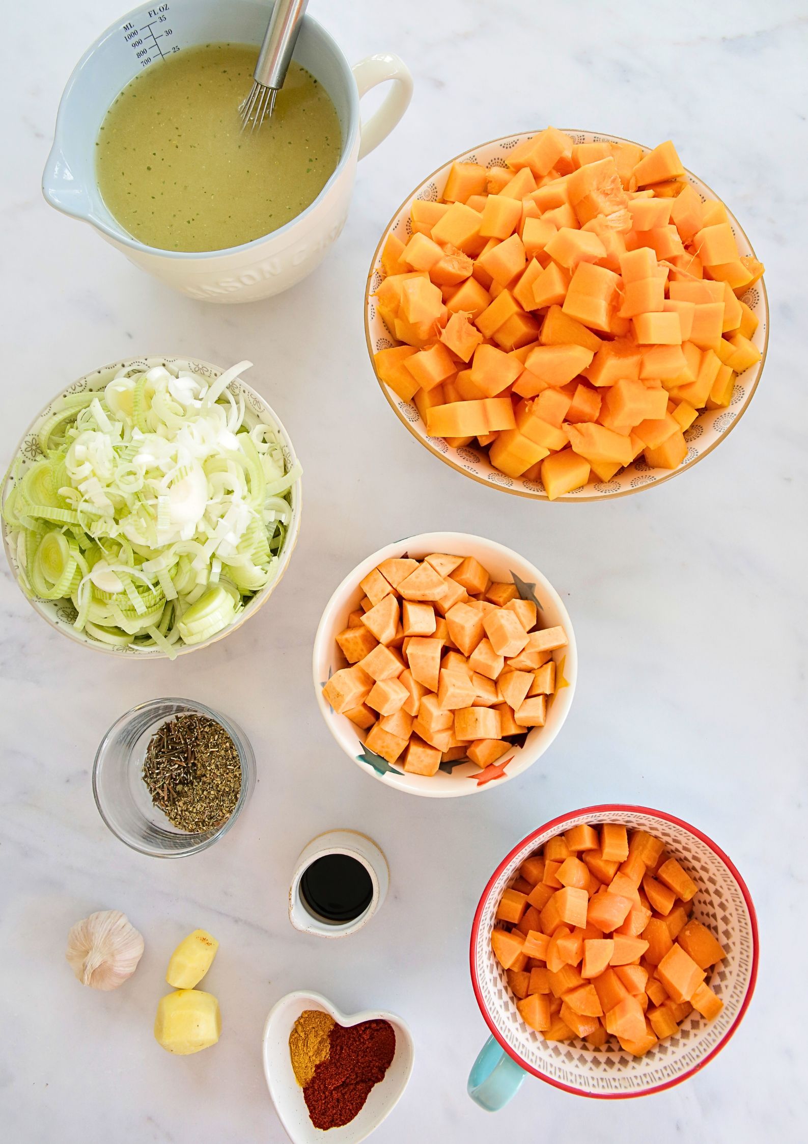 Top down photo of prepared vegetables, herbs, spices and stock in different bowls