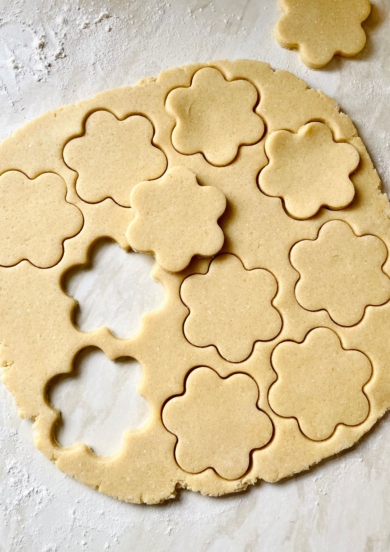 Rolled-out vegan cookie dough with flower-shaped cookies cut out, resting on a lightly floured surface