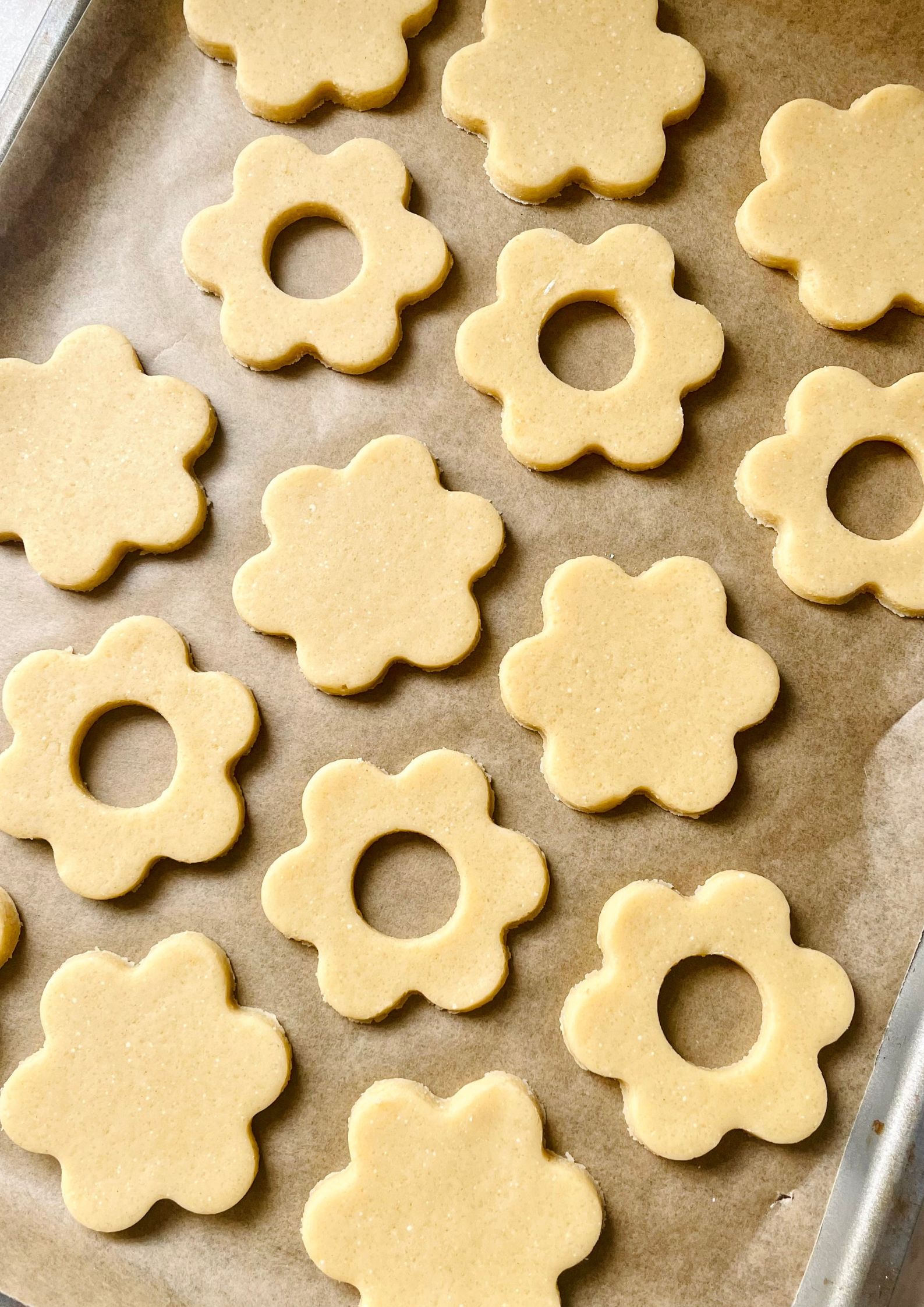 Flower shaped vegan cookies sitting uniformly on parchment on a baking tray ready to be baked.