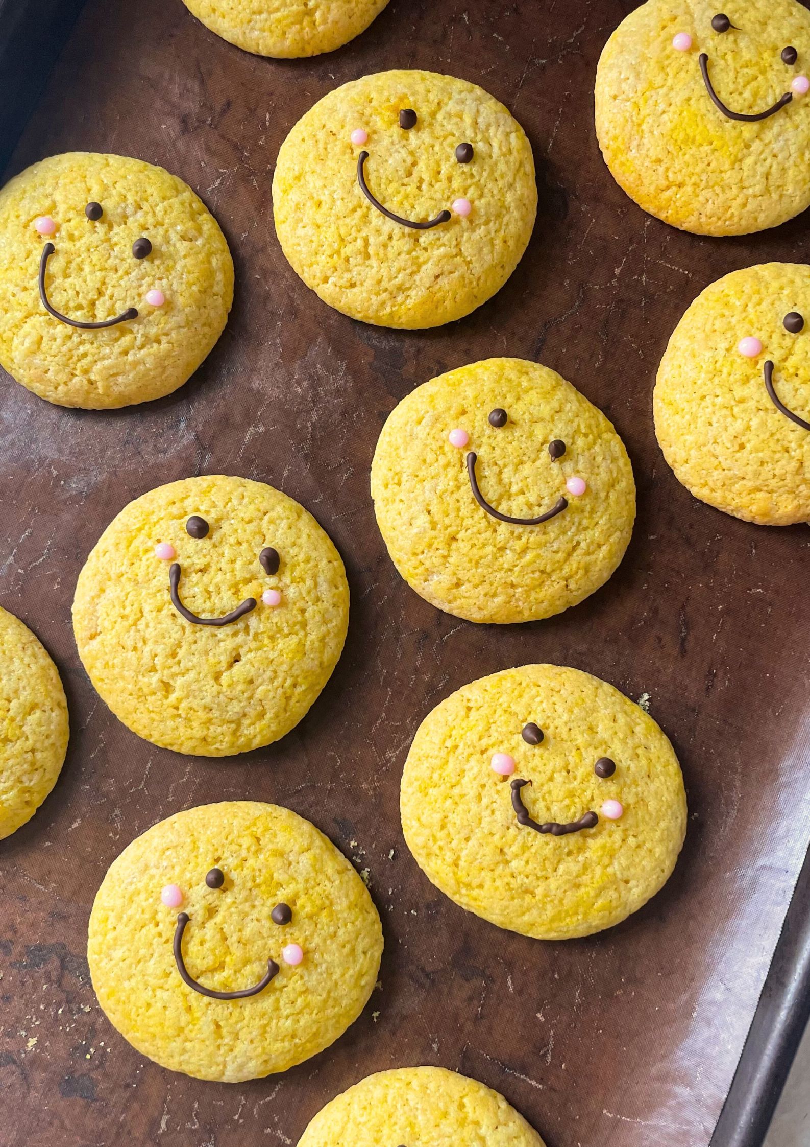 Flat lay of decorated yellow cookies with a chocolate smiley face and pink icing 'cheeks'